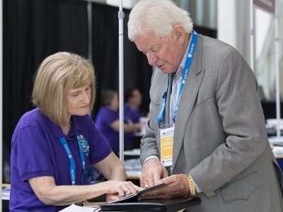 Volunteer assisting SLC 2026 attendee at registration desk.