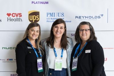 SLC 2026 attendees in front of sponsor sign.