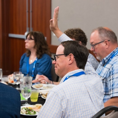 SLC 2026 attendee with raised hand during a conference luncheon.