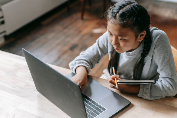 Young girl using a laptop and taking notes at a table.