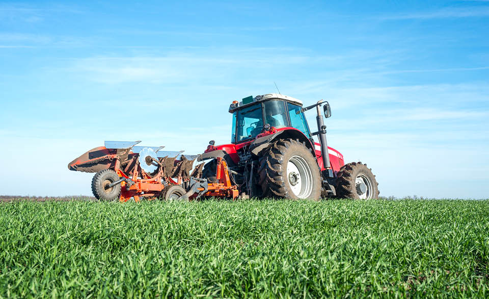 Red tractor plowing a green field with farming equipment attached.
