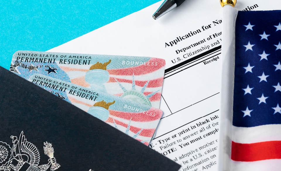 U.S. permanent resident cards and immigration application paperwork next to a passport and American flag.