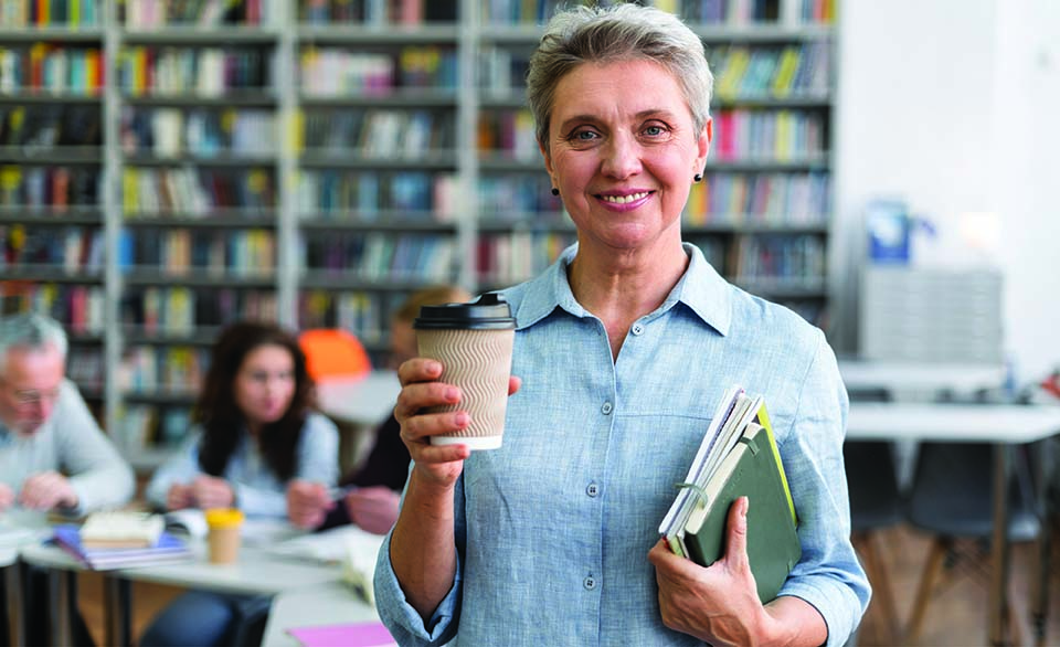 Education leader holding books in a library setting, representing principal licensure, qualifications, and school leadership.
