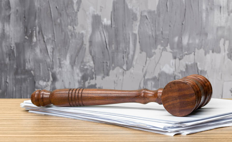 Wooden judge’s gavel resting on a stack of legal documents on a desk.
