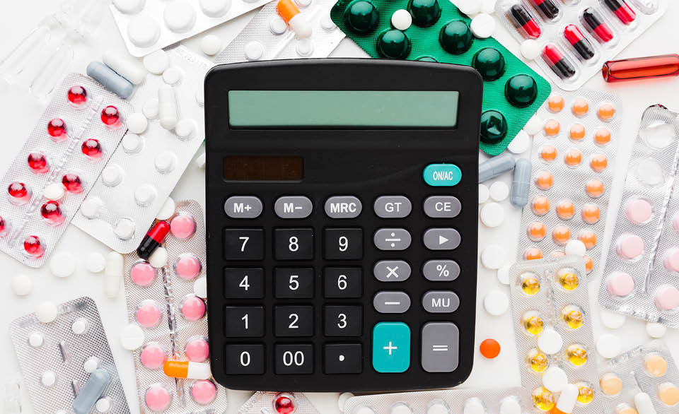Calculator surrounded by various prescription pills and blister packs, representing medication costs or healthcare expenses.