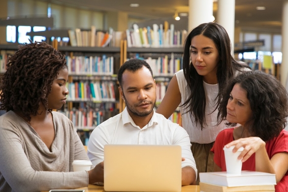 Adults working together around a laptop in a library.