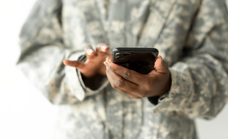 Person in a camouflage uniform uses a smartphone.